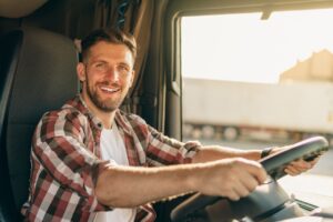Professional middle aged truck driver in casual clothes driving truck vehicle going for a long transportation route.