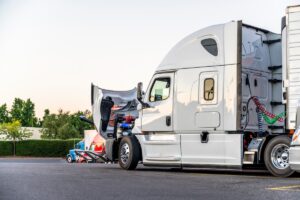 White bonnet big rig semi truck with open hood for engine inspection and possible mobile repair standing on the truck stop parking lot on row with another semi trucks