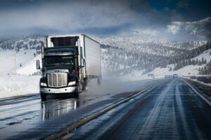 Semi truck driving along a road in winter with snowy surroundings