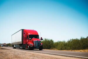Red semi-truck driving along road against clear blue sky