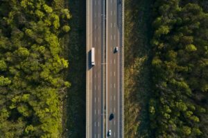 Car traffic moving on highway, aerial view. Countryside road through forest