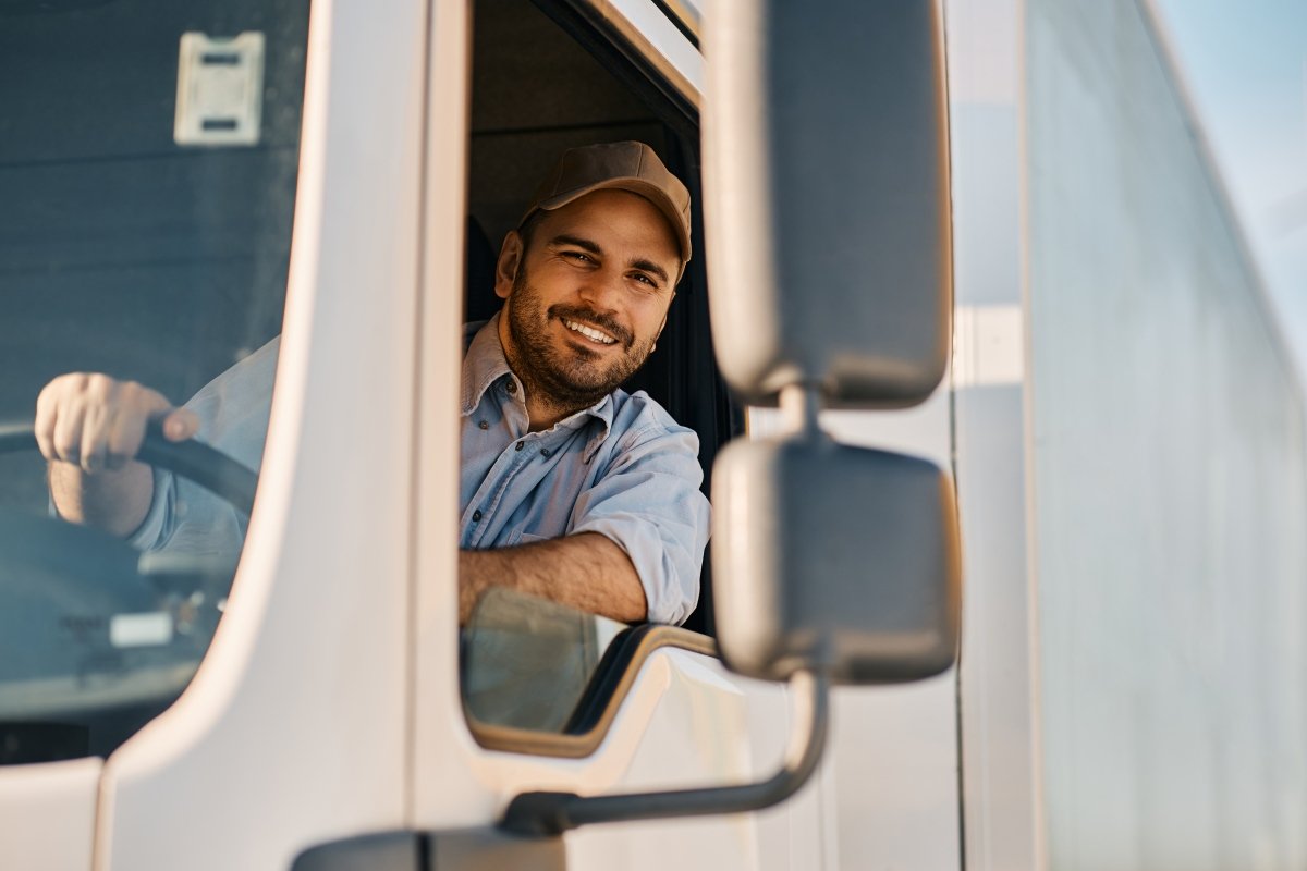 Happy professional truck driver driving his truck and looking at camera.