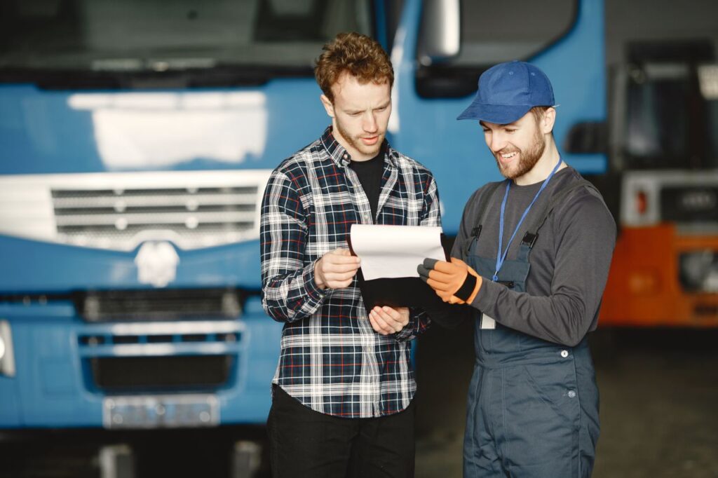 Two men reviewing loan paperwork in front of a commercial truck during a vehicle inspection