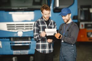 Two men reviewing loan paperwork in front of a commercial truck during a vehicle inspection