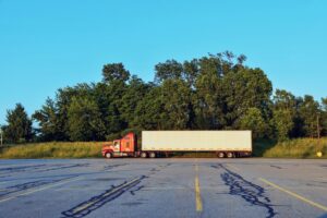 Red semi-truck with a white cargo trailer parked in an empty lot at golden hour, representing the older commercial trucks owner-operators often finance