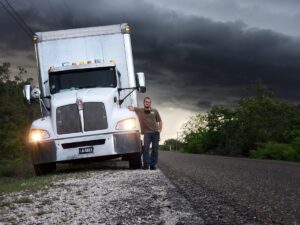 truck driver leaning against truck next to road with dark cloudy background