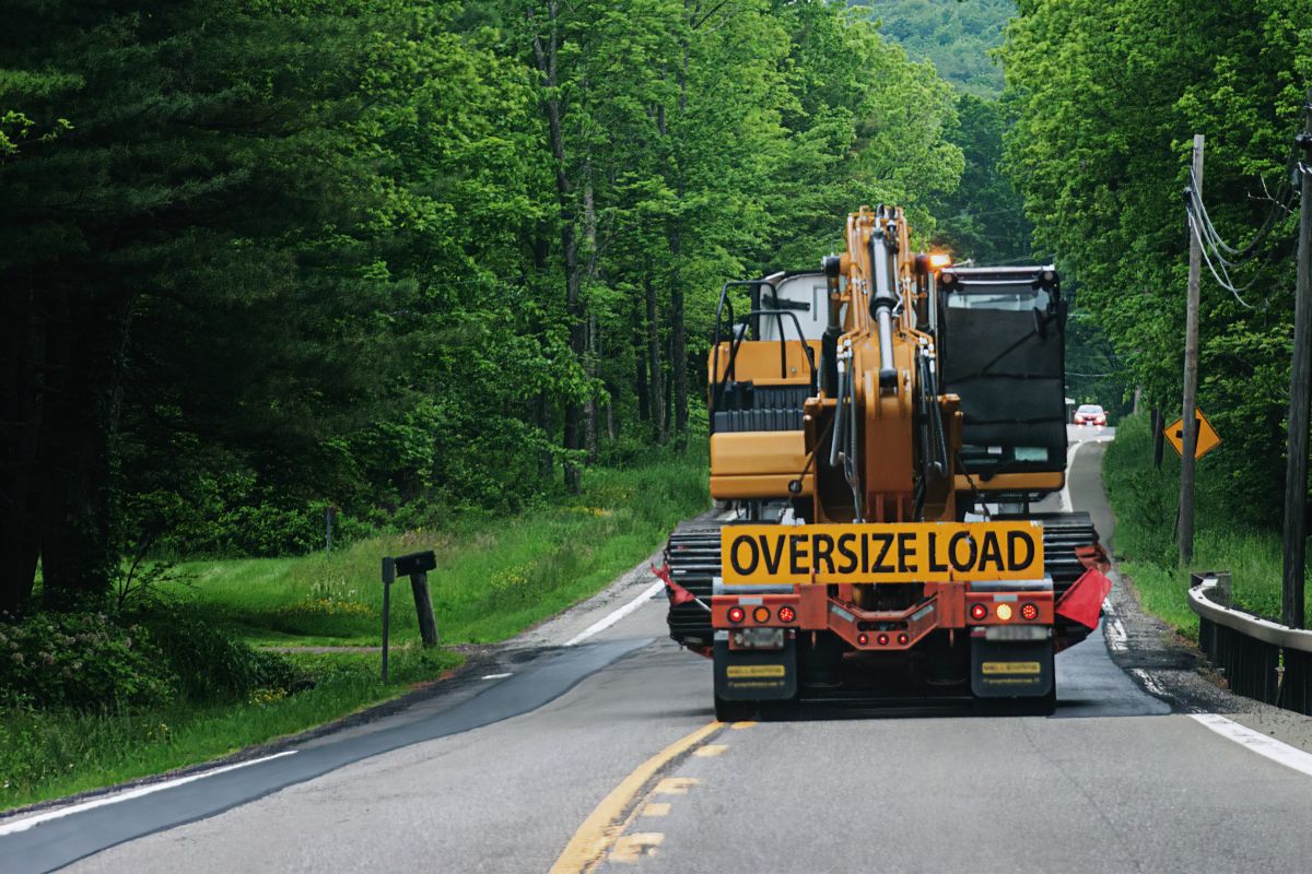 A truck carrying an oversize load is heading toward an oncoming car on Route 79 in the small town of Windsor in Broome County in Upstate NY. Taking up 2 lanes of rural road.