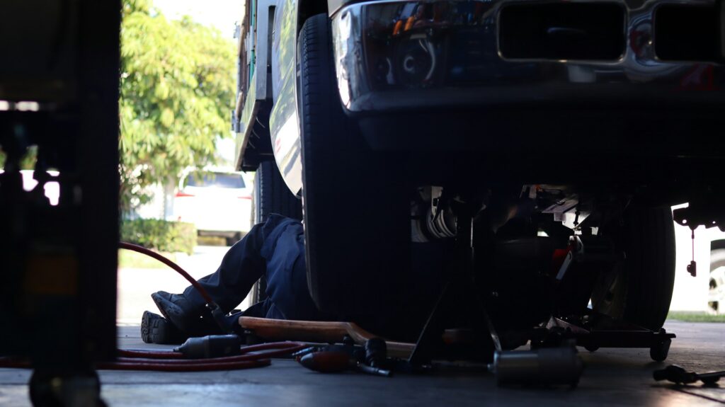 Mechanic lying under a semi truck inspecting the driveshaft and undercarriage with pneumatic tools