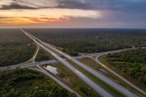 Elevated view of freeway exit junction over road lanes with fast moving traffic cars and trucks at sunrise. Interstate transportation infrastructure in USA.