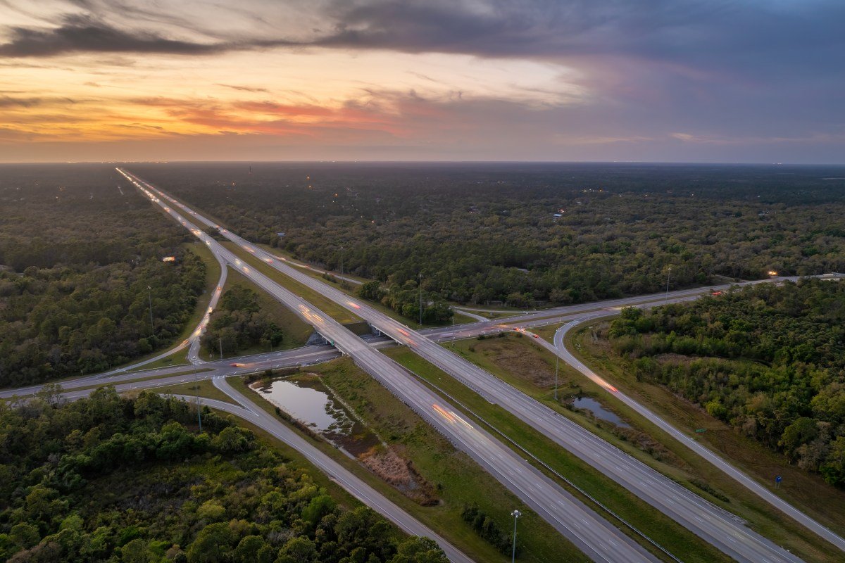 Elevated view of freeway exit junction over road lanes with fast moving traffic cars and trucks at sunrise. Interstate transportation infrastructure in USA