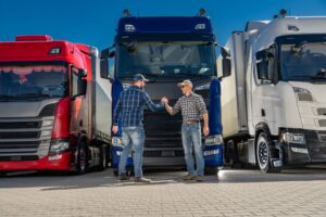 two truck drivers shaking hands in front of a truck