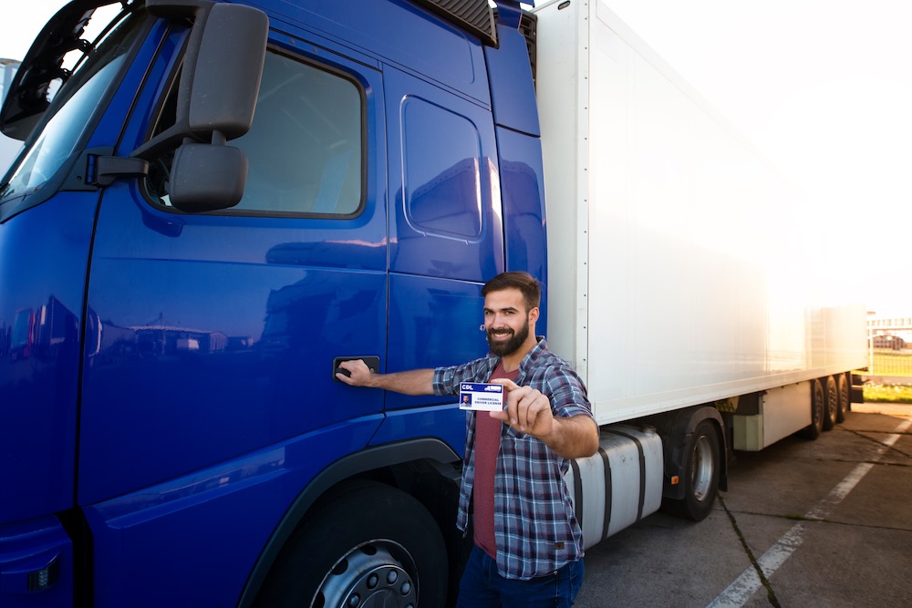 Truck driving school. CDL training for truck drivers. Professional truck driver standing by his truck and holding commercial driving license. Transportation service.