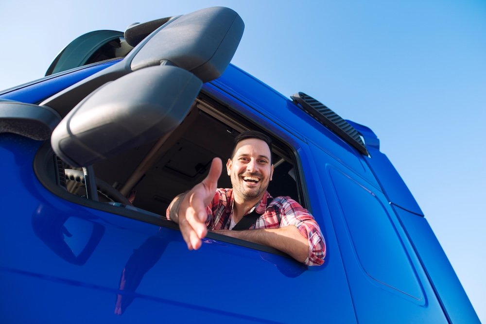 Truck drivers job openings. Truck driving careers. Middle aged professional trucker driver sitting in his vehicle cabin and giving shaking to new recruits. Drivers wanted.
