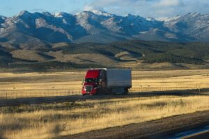 Red truck driving in open area with mountain backdrop