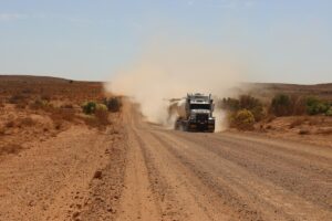 truck driving along a dirt road with sand blowing out