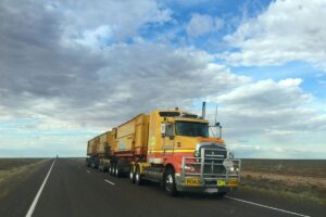 Yellow truck driving on open road with cloudy blue sky background