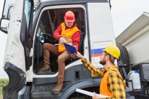 Truck driver brings delivery to construction site from road construction with worker