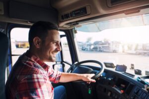 Professional middle aged truck driver in casual clothes driving truck vehicle going for a long transportation route.