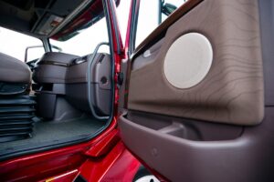 The interior of a modern luxury red semi truck made in shades of brown plastic. Through the open door with wood paneling truck visible part of the seat with shock absorbers and the dashboard console with air vents.