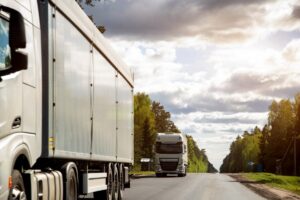 A column of trucks with semi-trailers transports cargo along a country road.