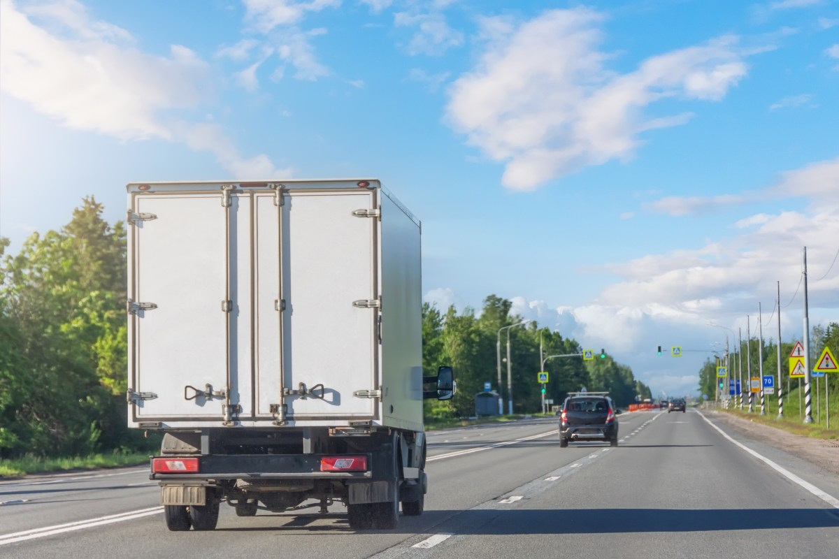 Mini truck driving on highway on sunny day. White modern delivery small shipment cargo courier truck moving fast on motorway road to city urban suburb. Busines distribution logistics express service.