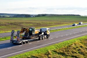 Trailer truck with long platform transporting Excavator on highway.