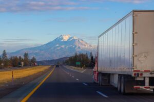 A semi tractor trailer truck drives on the Interstate in California with Mount Shasta in the distance at Sunset.