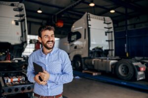 Smiling truck owner standing in auto park and holding tablet.