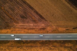 Cars and trucks on the straight road through plain countryside landscape, aerial view from drone pov