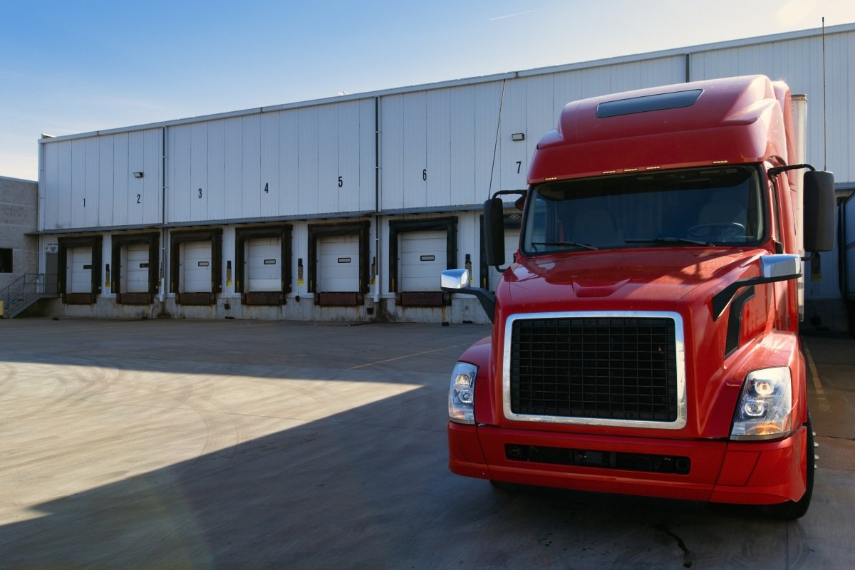 Red modern American semi truck parked at the docks, waiting to get loaded. Shipping and receiving, transportation business concept. Truck driving jobs.