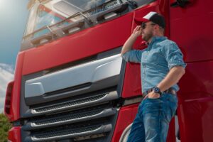 Caucasian Euro Semi Truck Driver in Front of His Brand New Red Truck Tractor.