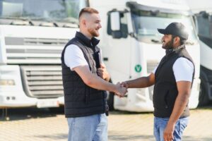 Two diverse truck drivers making a business deal and handshaking in front of semi trucks, celebrating a successful collaboration