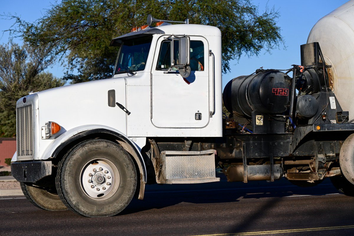 White concrete mixer truck driving on a paved road, representing commercial construction transportation equipment used for mixing and delivering cement materials