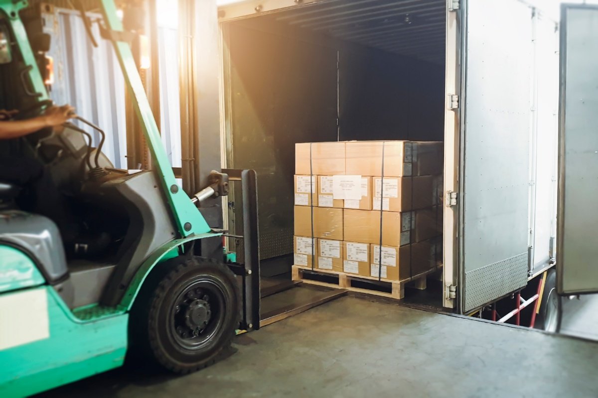 Green forklift moving cargo into the back of a box truck