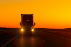Semi truck driving directly into camera at sunset with lights flaring