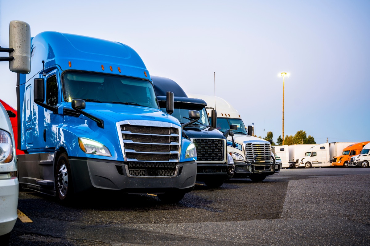 Different big rigs semi trucks standing in row on the truck stop