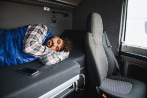 Truck driver resting and sleeping in the comfortable bunk area of the semi truck cabin during a long haul journey