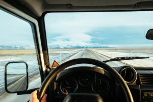 Driver's view from inside a semi-truck cab, hands on the wheel on an open winter highway.