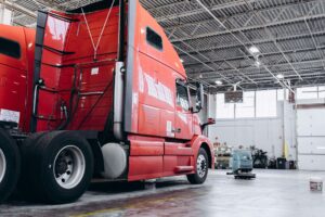 Red semi-truck cab with raised sleeper compartment parked inside a maintenance shop bay