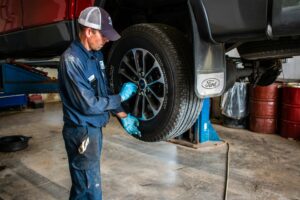 Mechanic in coveralls and blue gloves servicing a wheel on a lifted pickup truck in a repair shop