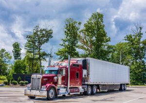 Red cab truck with white reefer trailer parked in front of trees