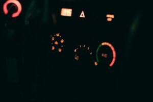 A close-up of a dark semi truck dashboard showing illuminated warning lights, including a hazard triangle icon and digital display.