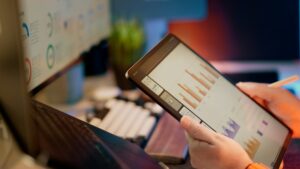 A hand holds a tablet displaying bar charts and performance data, used for tracking fleet maintenance costs and KPIs.