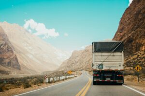 Rear view of a semi truck hauling a covered trailer on a two-lane highway through a desert mountain pass