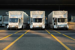 Three white box trucks parked side by side at loading dock bays, front view in evening light