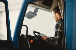 Truck driver sitting in the cab of a semi truck reviewing paperwork on a clipboard before a trip