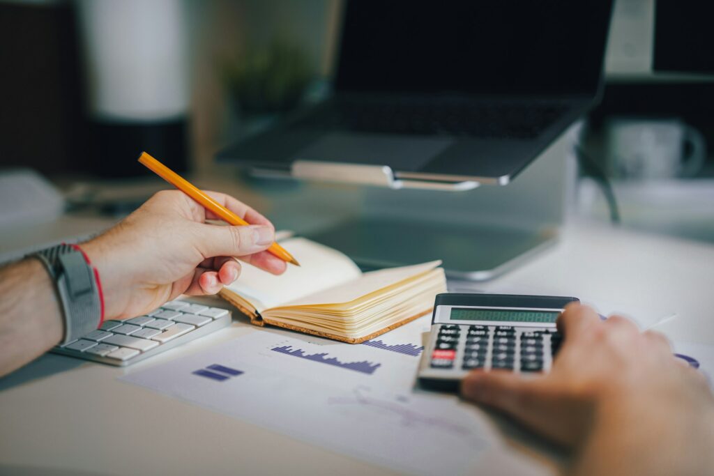 Person holding a pencil over a notebook while using a calculator to add up truck loan fees and costs