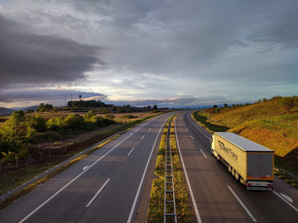 Semi truck with a curtain-side trailer driving on an empty divided highway under a cloudy sky