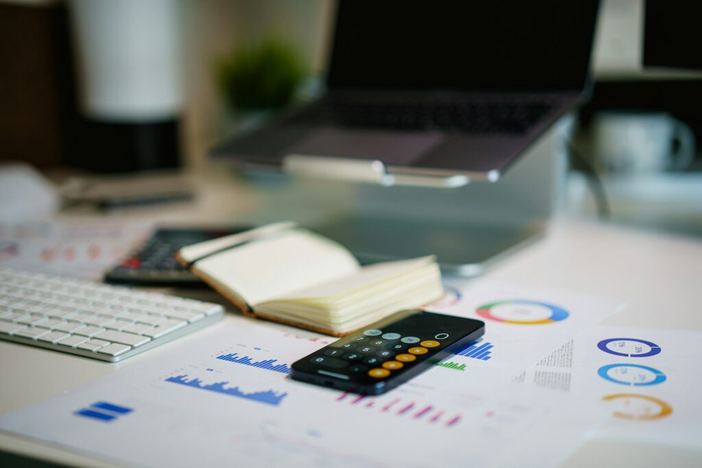 Smartphone calculator on printed financial charts beside a notebook and laptop, used to work out hidden costs in truck financing