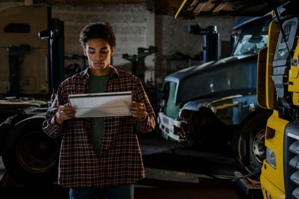 Technician in a plaid shirt inspects a truck air filter in a repair shop during preventive maintenance